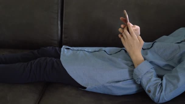 身着蓝色连衣裙的少女躺在一个靠着智能手机的手中 年轻女孩滚动在社交媒体上 青少年成瘾 — 图库视频影像