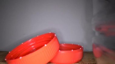 Kamera ahşap arka plan üzerinde şişe kapakları ile yalak boş plastik şişe ler sürgülü. Şeffaf, yeniden kullanılabilir plastik atıklar. Plastik geri dönüşüm, çevre sorunları