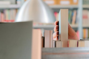 Kütüphanedeki raftan kitap seçen genç bir öğrenci. Sınavlara hazırlanmak, üniversitede halk kütüphanesinde kitap arayan veya seçen genç adam