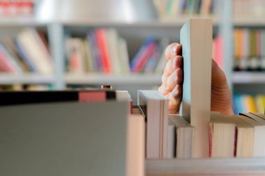 Kütüphanedeki raftan kitap seçen genç bir öğrenci. Sınavlara hazırlanmak, üniversitede halk kütüphanesinde kitap arayan veya seçen genç adam