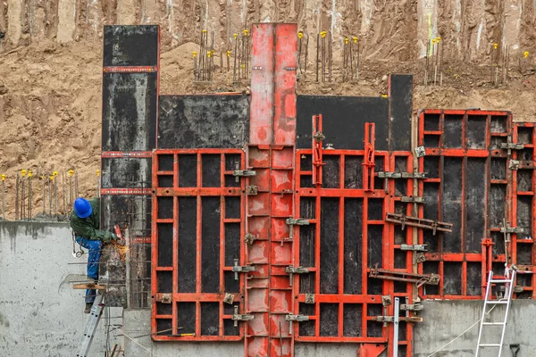 Строитель работает на строительном фундаменте. Человек в синей рабочей одежде на лестнице паяльник металл для укрепления бетонной стены структуры на склоне холма — стоковое фото