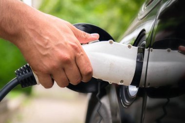 Yeşil ortamda elektrikli arabaya mans el takma şarj cihazı fişi. Yeni enerji aracı, Nev elektrik enerjisi ile yükleniyor. Ekoloji, günümüz arabaları