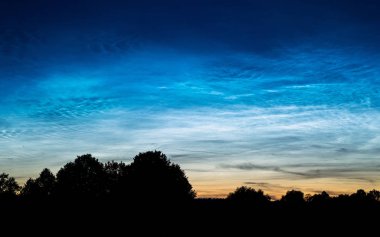 Şehrin dışındaki kırsal bir manzarada gece gökyüzünde gümüş bulutlar olarak da bilinen nadir Noctilucent bulutlar. Bu fenomen bulutlar buz kristallerinden oluşur ve astronomik alacakaranlık sırasında görülebilir