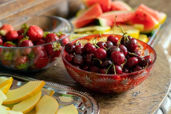 Fresh summer fruits: cherries, organic strawberries, melon slices, water melon in vintage crystal bowl on old wooden table