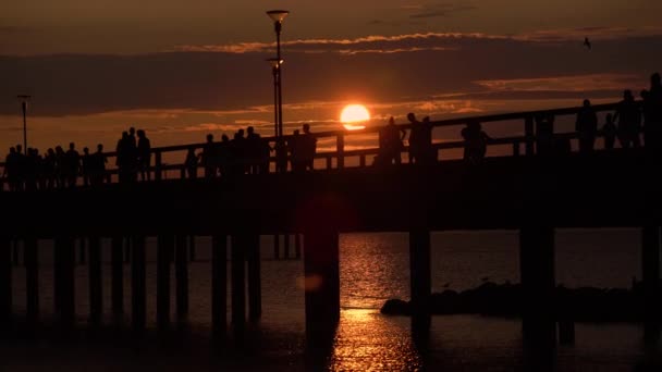 在炎热的夏日 在立陶宛帕兰加海滩 人们在戏剧性的日落时沿着码头漫步 五颜六色的日落进入波罗的海 而游客享受温暖的天气在热门度假胜地 — 图库视频影像