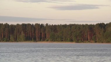 Arka planda orman ile göl kenarında sakin bir akşam. Su kıyısında gün batımı gökyüzü. Doğada huzurlu zaman kamp