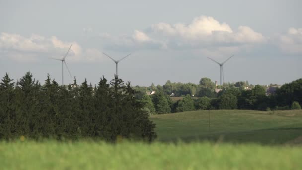 木々や草に囲まれた遠くに風力タービンを回転させる 自然と雲に囲まれた田舎の村の回転風車 — ストック動画