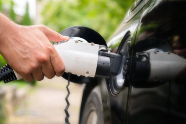 Yeşil ortamda elektrikli arabaya mans el takma şarj cihazı fişi. Yeni enerji aracı, Nev elektrik enerjisi ile yükleniyor. Ekoloji, günümüz arabaları