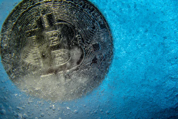 Silver Bitcoin, bit coin online digital currency frozen in the blue ice. Concept of block chain, crypto market crash. Frozen crypto money, depreciation