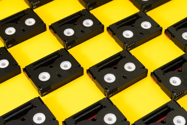 Vintage mini DV cassette tapes used for filming back in a day. Pattern made of plastic video tapes on yellow background