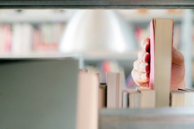 Kütüphanedeki raftan kitap seçen genç bir öğrenci. Sınavlara hazırlanmak, üniversitede halk kütüphanesinde kitap arayan veya seçen genç adam