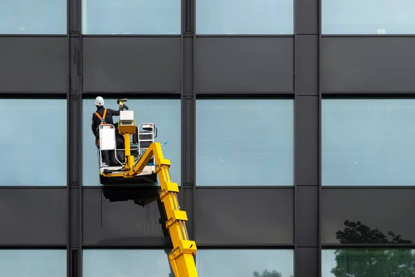Mannelijke ruitenreiniger die ramen schoonmaakt op modern gebouw hoog in de lucht op een liftplatform. Werknemer polijsten glas hoog in de lucht — Stockfoto