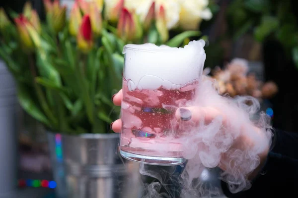 Beautiful woman holding dry ice cocktail at the party. Purple cocktail drink with ice vapor at the club