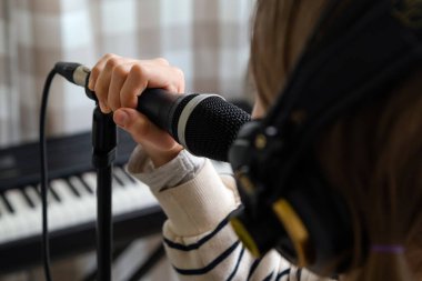 Ev stüdyosunda müzik kaydeden bir gencin yakın çekimi. Kulaklık takan ve mikrofon kaydı yapan kız.
