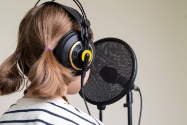 Ev stüdyosunda müzik kaydeden bir gencin yakın çekimi. Kulaklık takan ve mikrofon kaydı yapan kız.