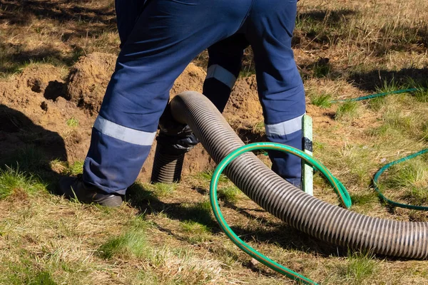 Boru tutan işçi, dışarıdaki kanalizasyon temizleme servisini sağlıyor. Kanalizasyon pompalama makinesi tıkanmış rögar kapağını açıyor