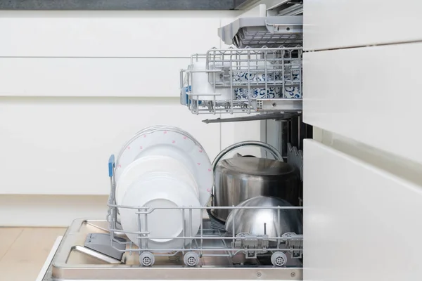 Cleaning dishes - plates, cups and other kitchen tools at dish washer. Full shelf of kitchen appliances in a dishwasher. Nobody
