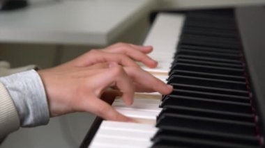 Ev müziği stüdyosunda piyano çalan bir gencin yakın çekimi. Çevrimiçi dersi alan ve modern elektrikli piyano üzerinde pratik yapan bir kız.