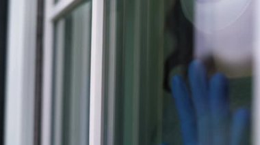 Kadınlar, içeride pencerenin yanında tıbbi eldivenlerle el ele tutuşuyorlar. Ev izolasyonu. Corona virüsü. Evde kal..