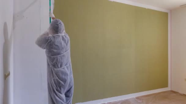 Zeitraffer des Malers, der die Wand weiß anstreicht. Mann in Schutzkleidung dekoriert den Raum mit einer Farbrolle. Haussanierung. Wohnungserneuerungskonzept.