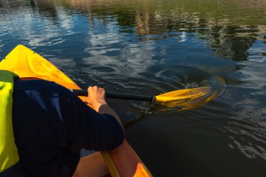 Güneşli bir günde nehirde kano sürerken yakın çekim. Eller kürek çeker ve akan suda kürek çeker.