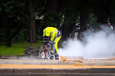 İnşaat işçisi arkasında toz bulutuyla sokakta tuğla kesiyor. Kentsel gelişim