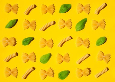 Sarı arka planda pişirilmemiş kıvırcık makarna ve fesleğen yaprağı deseni. Geleneksel çiğ makarna kalıbı. Kimse.