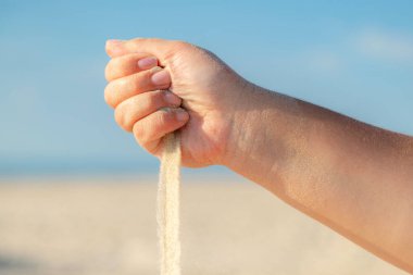 Güneşli bir yaz gününde kumsaldaki elden dökülen kumlara yakın. Tatilde kumla oynamak.