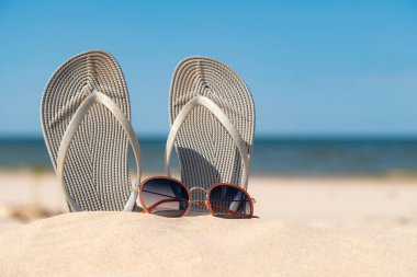 Güneşli bir günde kumsalda gri sandaletler. Deniz kenarındaki kumda terlikler. Okyanus kıyısında takla atıyor..