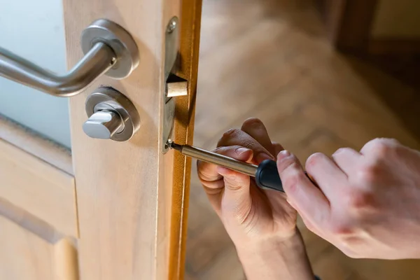 Carpenter repairing door lock. Installing a door handle. Handyman tightening door hinge . Hands of the repairman with a screwdriver. Locksmith screwing bolt into wooden door