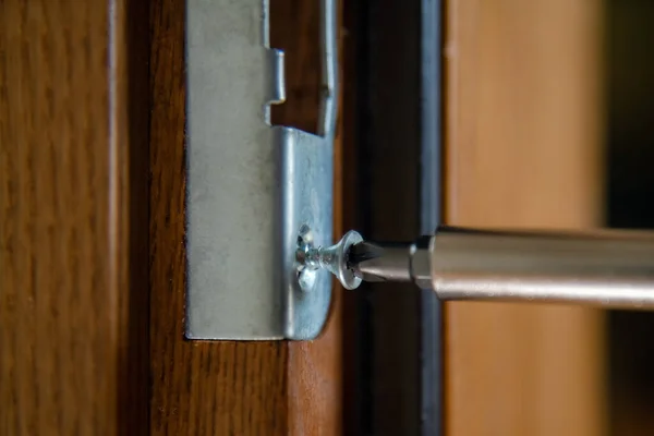 Close up of carpenter repairing door lock. Installing a door handle. Handyman tightening door hinge . Hands of the repairman with a screwdriver. Locksmith screwing bolt into wooden door