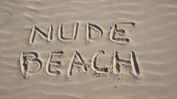 砂の上に書かれたヌードビーチの看板でブラジャーを投げる女性の閉じるまで 砂浜で裸で日光浴の概念 自然主義的なライフスタイル — ストック動画