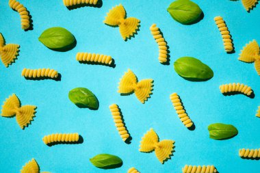 Mavi arka planda pişirilmemiş kıvırcık makarna ve fesleğen yaprağı deseni. Geleneksel çiğ makarna kalıbı. Kimse.