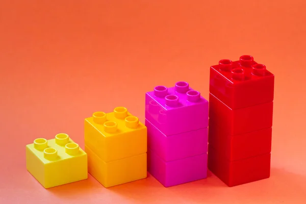 Growing bar chart from color toy blocks on red background. Closeup.