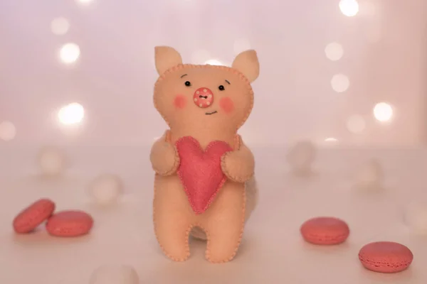 心のあるフェルト製手作りベージュ豚新年のライト ピンクのマカロンとボールの背景の上に立つ — ストック写真