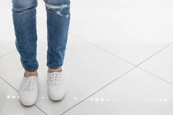 Ноги в джинсах і білі кросівки стоять на підлозі білої плитки в магазині взуття . — стокове фото