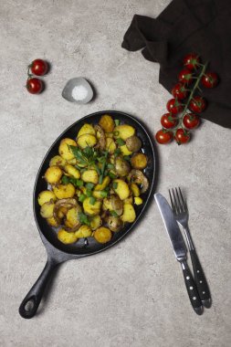 Kızarmış patates mantar ve soğan demir tava, cherry domates, bıçak ve çatal, tuz ve gri arka plan, yakınındaki peçete