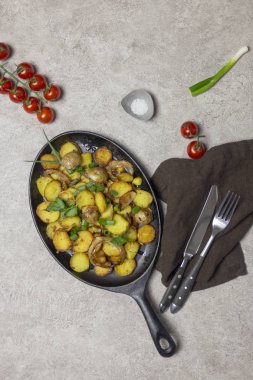 Kızarmış patates mantar ve soğan demir tava, cherry domates, bıçak ve çatal, tuz ve gri arka plan, yakınındaki peçete