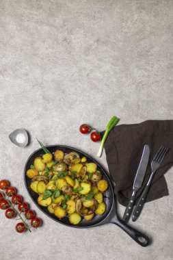 Kızarmış patates mantar ve soğan demir tava, cherry domates, bıçak ve çatal, tuz ve gri arka plan, yakınındaki peçete