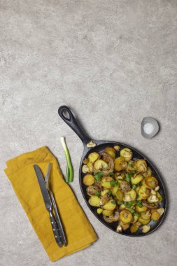 Şükran günü yemeği. Kızarmış patates mantar ve soğan demir tava, cherry domates, bıçak ve çatal sarı peçete, yeşil soğan ve tuz gri arka plan