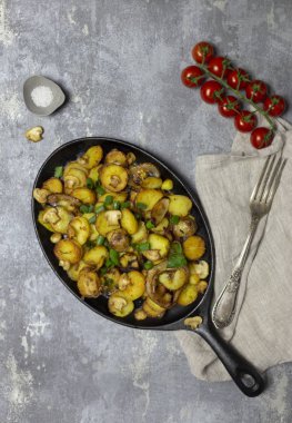 Tatil yemek. Rustik tazelik kızarmış patates mantar ve soğan çatal, tuz, domates ve gri arka plan, peçete ile demir tavada