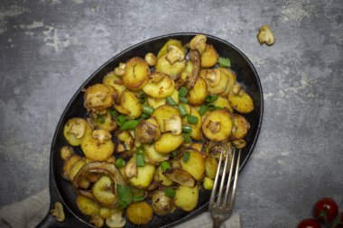 Rustik tazelik kızarmış patates mantar ve demir tavada gri arka plan, çatal ile soğan