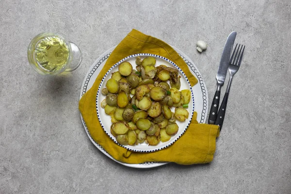 Table setting for holiday dinner. Fried potatoes with mushrooms and onion at light background. Yellow napkin, fork and knife, fresh mushroom and glass of white vine near.