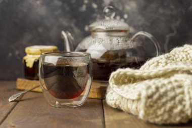 Çaydanlık ve yakınındaki, örme battaniye ile cam fincan çay kaşıkla ahşap arka plan, kavanoz reçel ile.