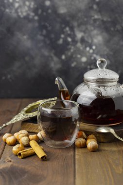 Çaydanlık ve örme battaniye yakınındaki, vanilya pod ve fındık, tahta arka plan ile kaşık ve süzgeç yakınındaki ile cam fincan çay.