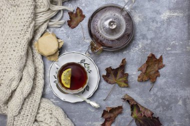 Siyah çay ve limon ve tabak, kaşık, jöle kavanoz, akçaağaç yaprakları ve yakınındaki örme eşarp, gri bir arka plan ile Kupası