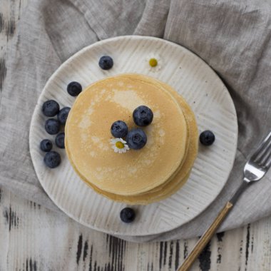 Beyaz tabak çatal gri havlu ve beyaz tahta arka plan ile yaban mersinli krep yığını