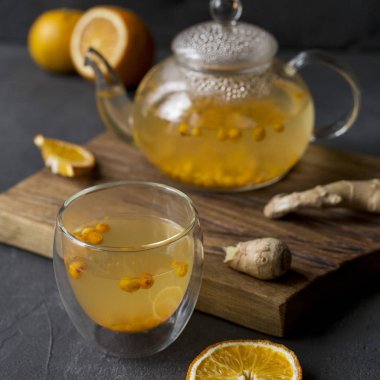 Sıcak deniz buck diken çay cam çaydanlık cam fincan, turuncu ve siyah arka plan üzerine ahşap panosu yakınındaki, zencefil