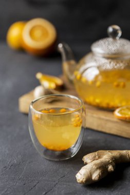 Sıcak deniz buck diken çay cam çaydanlık cam fincan, turuncu ve siyah arka plan üzerine ahşap panosu yakınındaki, zencefil