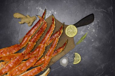 Taze limon dilimleri, zencefil, tuz ve biberiye siyah arka plan üzerine ahşap panosu ile Kamçatka yengecin pençe Kral